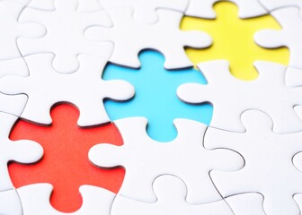 Obraz premium An incomplete white jigsaw puzzle with three missing pieces, each in a different primary color: blue, red, and yellow