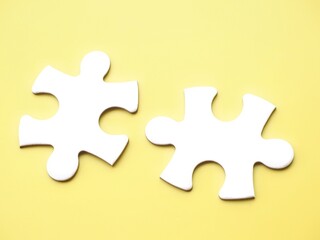 Fototapeta premium Two complementary white jigsaw puzzle pieces on a yellow background, symbolizing association, connection, or interdependence. Copy space to add text