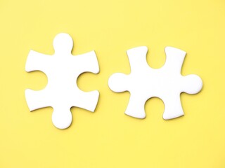 Two complementary white jigsaw puzzle pieces on a yellow background, symbolizing association, connection, or interdependence. Copy space to add text