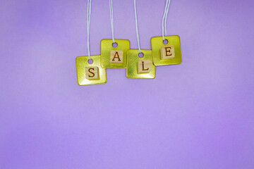 重なった金色のタグにセールの英語ブロックを飾った紫の背景