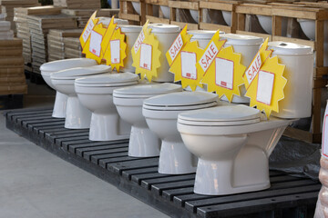 A row of toilets are on display with yellow signs that say 