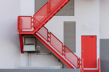 A red staircase with a white building in the background. fire escape ladder outside of building.