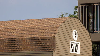A brown and tan barn with a white window. rubber roof shingle.