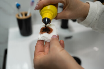 Close-up of unrecognizable young woman's hands applying iodine drops to sterile gauze for wound...