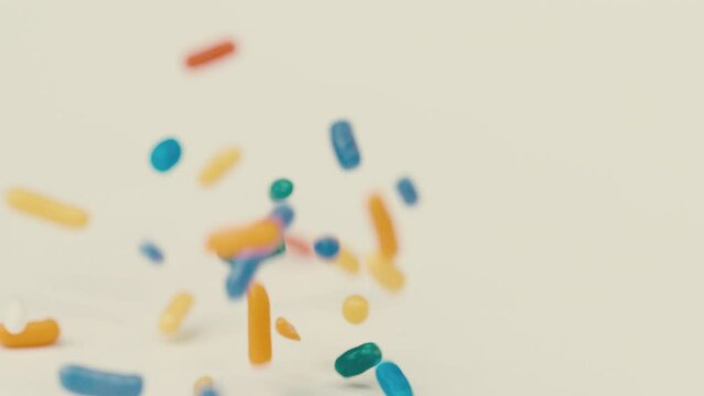 Multicolor rainbow sprinkles land on white table and bounce in all directions in slow motion