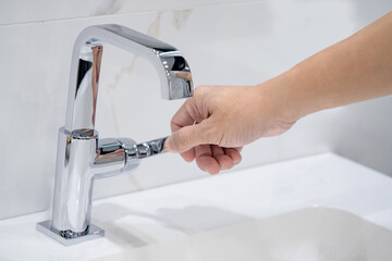 Male hand closing water tap over the white ceramic wash basin. Modern stainless steel or chrome...