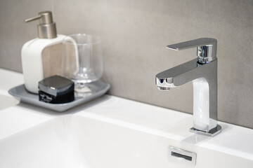 Chrome water tap on white ceramic wash basin with bathroom accessories set. Modern stainless steel...