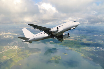 White airplane flying in the sky among white dense clouds floating over land surface. Travel background