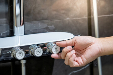 Customer hand adjusting knob on shower mixer at home interior design showroom display. Choosing...