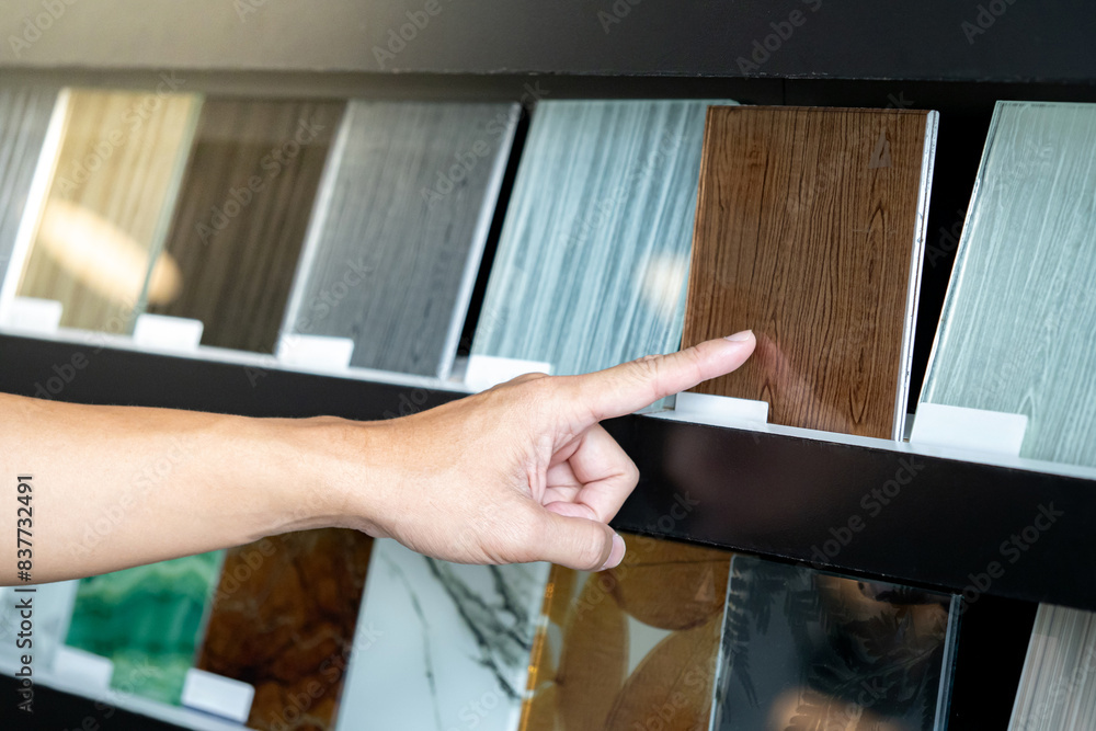 Wall mural architect hand choosing and pointing at brown tile material samples on the ceramic collection shelf 