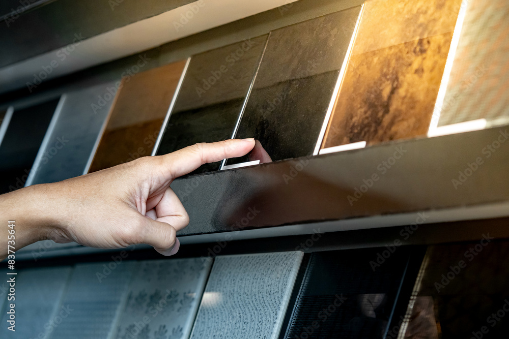 Wall mural architect hand choosing and pointing at black tile material samples on the ceramic collection shelf 