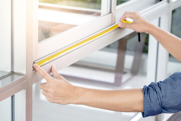 Male worker hands using tape measure checking dimension on aluminum window frame at construction...