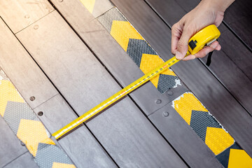Male worker hands using tape measure checking dimension on wooden stair step with yellow and black...