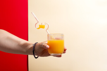 A woman is sitting at a table holding a glass of orange juice with a straw © YuliiaMazurkevych