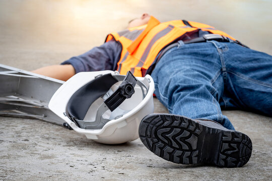 Accident and injury on a construction site. Safety first concept. Male worker lying down unconscious on the floor with safety helmet after falling from ladder. Fainting from exhaustion or heat stroke