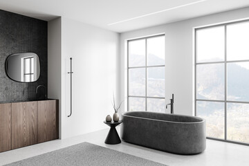 Minimalist bathroom with a dark bathtub and sink against a dark wall, light-filled room with large...