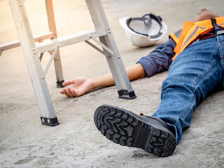 Accident and injury on a construction site. Safety first concept. Male worker lying down unconscious on the floor with safety helmet after falling from ladder. Fainting from exhaustion or heat stroke