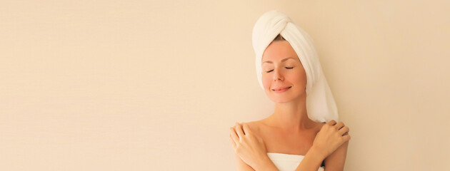 Beauty portrait of happy smiling young caucasian woman touches her clean skin while drying wet hair