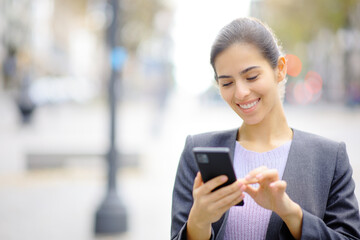 Young happy executive using phone in the street