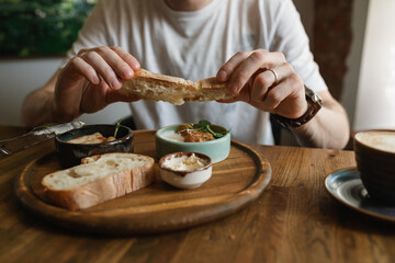 Close-up of man eating breakfast with  sausages, cauliflower fritters, bread, butter with a cup of coffee. 