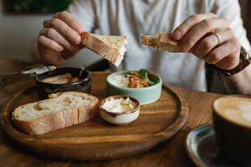 Close-up of man eating breakfast with  sausages, cauliflower fritters, bread, butter with a cup of coffee. 
