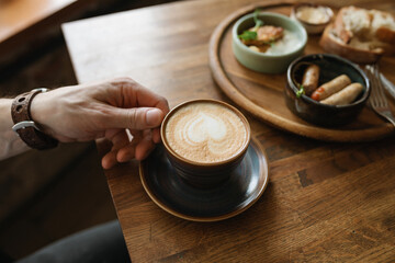 A close-up shot of a man enjoying a fragrant cup of freshly brewed coffee at a cafe during breakfast.