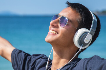 happy free young man with headphones on the beach breathing healthy air