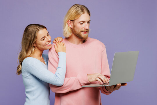Young fun couple two friends family IT man woman wear pink blue casual clothes together hold use work on laptop pc computer watch movie film isolated on pastel plain purple background studio portrait.