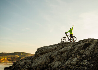 Carefree mature man standing with bicycle on rock at beach