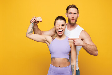 Young strong fitness trainer instructor sporty two man woman wear blue clothes spend time in gym point finger on biceps muscles on hand isolated on plain yellow background. Workout sport fit concept.