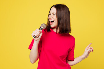 Young happy singer expressive Caucasian woman she wear pink t-shirt casual clothes sing song in microphone at karaoke club isolated on plain yellow orange background studio portrait Lifestyle concept