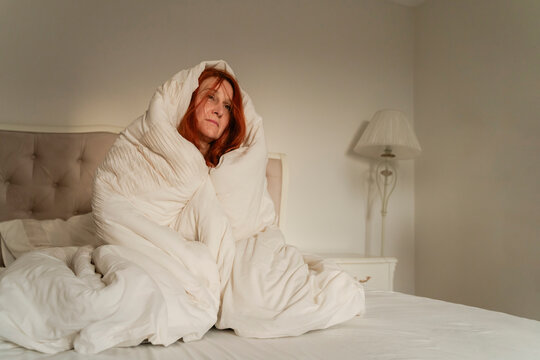 Alone woman wrapped in blanket sitting on bed at home