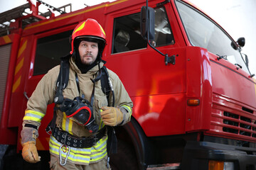 Firefighter in uniform near red fire truck at station