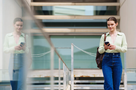 Woman walking and using smartphone near building