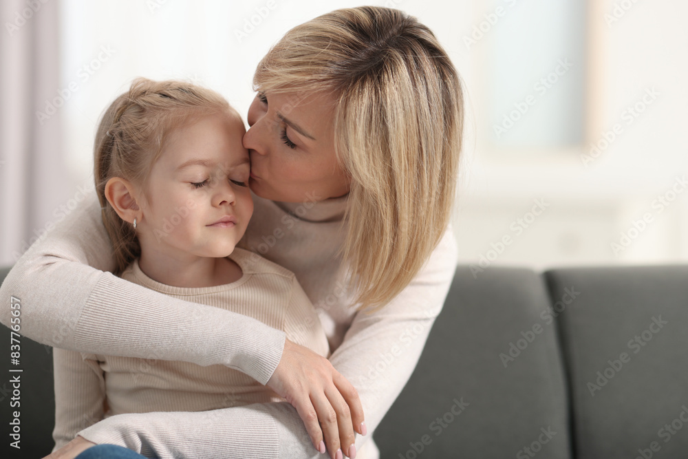 Poster Mother kissing her daughter on sofa at home. Space for text