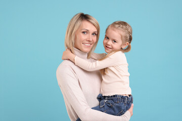 Daughter hugging her happy mother on light blue background
