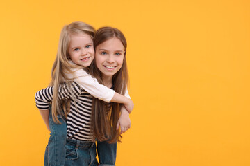 Portrait of cute little sisters on orange background, space for text