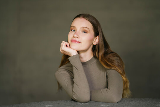Smiling woman with hand on chin sitting at table in front of gray wall