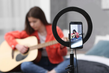 Obraz premium Teenage blogger playing guitar while streaming at home, focus on smartphone