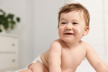 Cute little baby with moisturizing cream on face indoors