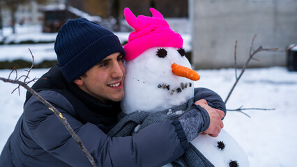 Close up Portrait of young man smiling and hugging a snowman