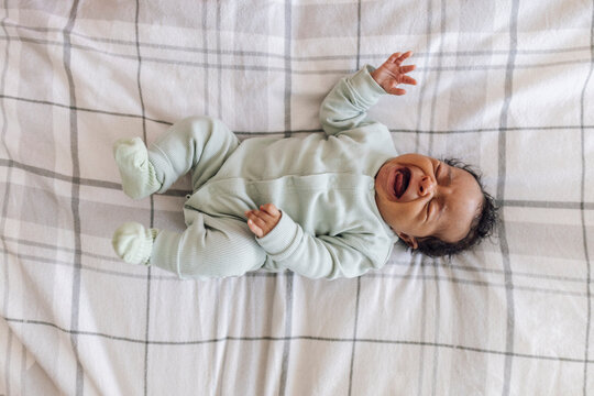 Crying baby girl lying down on bed at home