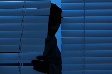 Thief looking out of blinds at night. Burglary