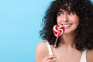 Beautiful woman with lollipop on light blue background, space for text