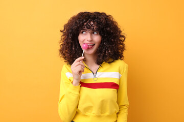 Beautiful woman with lollipop on yellow background