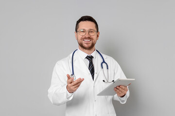 Portrait of smiling doctor with tablet on light grey background