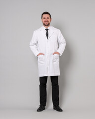 Full length portrait of smiling doctor on light grey background