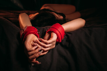 female hands in red leather BDSM handcuffs for submission and domination sex on a black sheet....