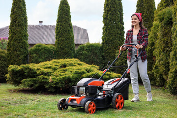 Smiling woman cutting green grass with lawn mower in garden