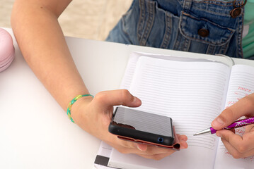 A person is multitasking with a cell phone and notebook, doing both at the same time